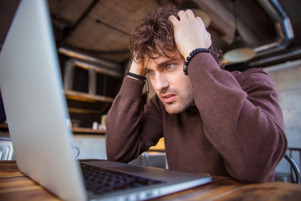 Stressful upset desperate handsome curly man in brown sweetshirt working using laptop and having headache Stressful upset desperate handsome curly man in brown sweetshirt working using laptop and having headache